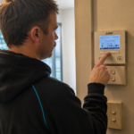 Morphett Air technician adjusting a Mitsubishi Electric wall controller set to 21°C in heating mode during winter.